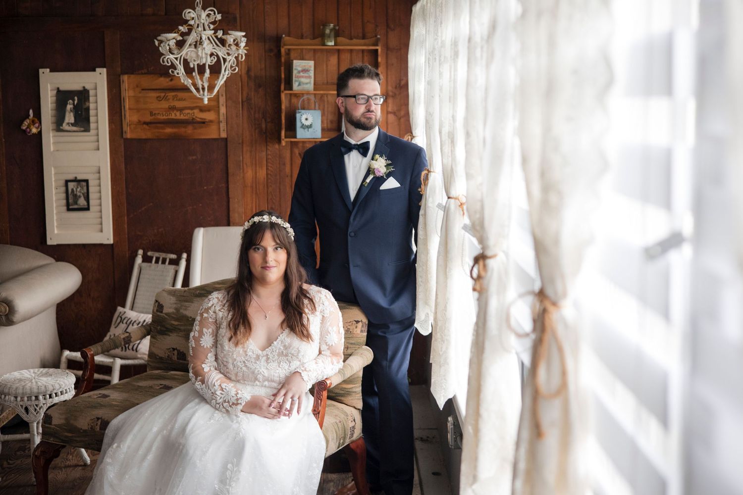 Couple poses in a rustic room with wooden walls, rocking chair and elegant chandelier on their wedding day.