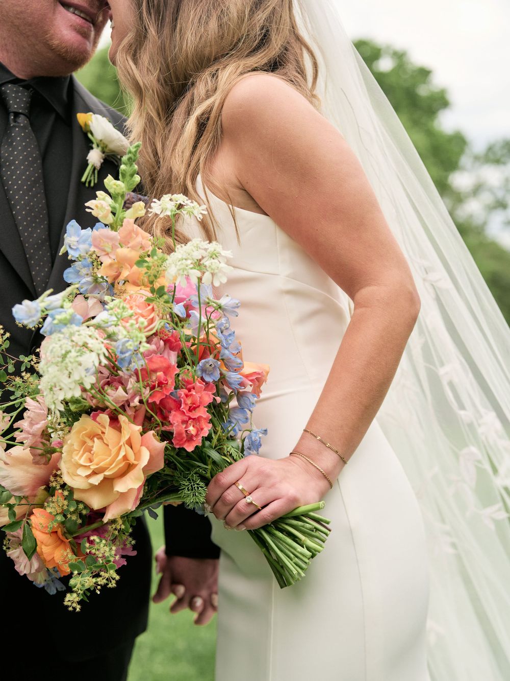 Colorful wedding bouquet with peach roses and mixed flowers held against a flowing white bridal gown.