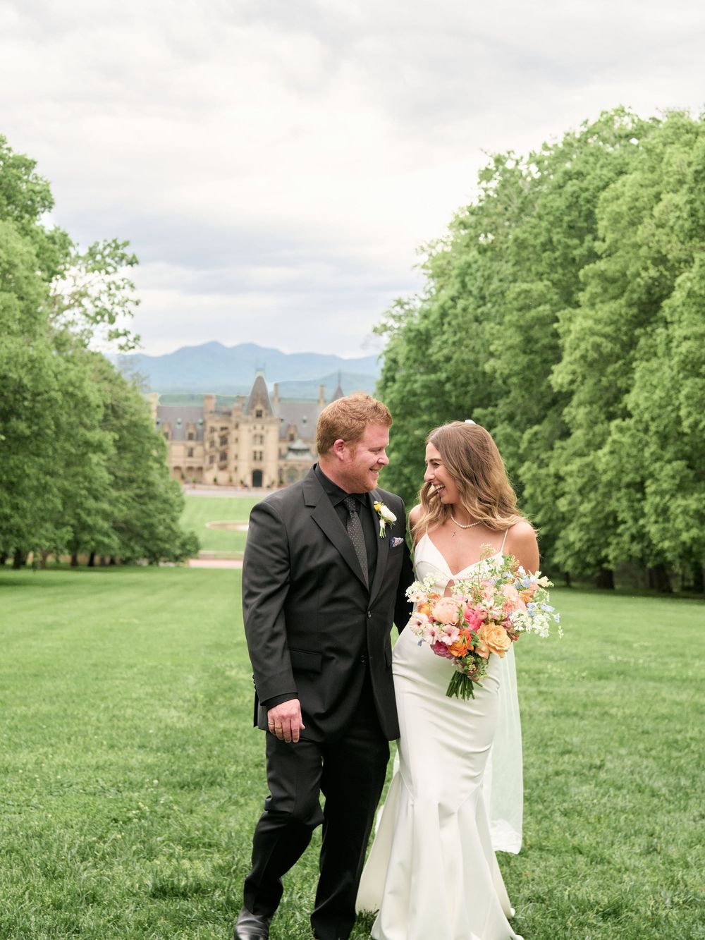 Wedding couple walking and laughing together on manicured grounds of a historic estate.