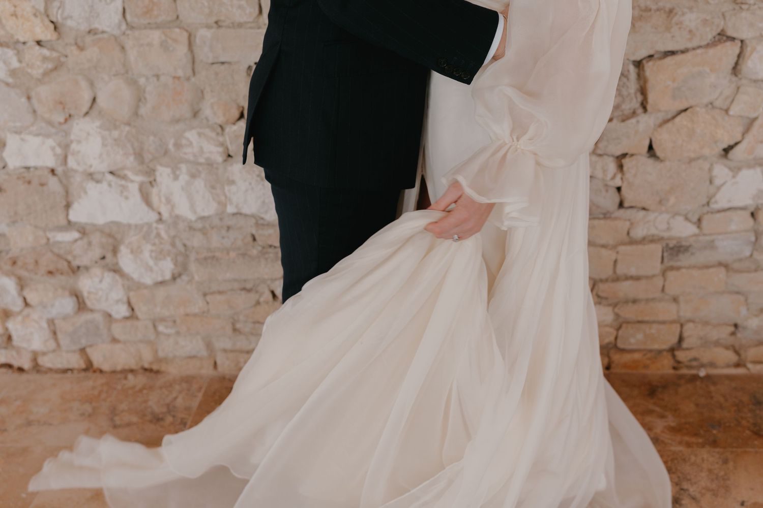 Couple de mariés photographié devant un mur ben pierre lors d'une séance photo mariage naturelle et élégante en Provence.