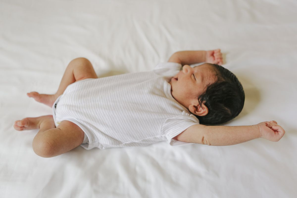 Baby stretching and yawning in bed, newborn lifestyle photography NYC