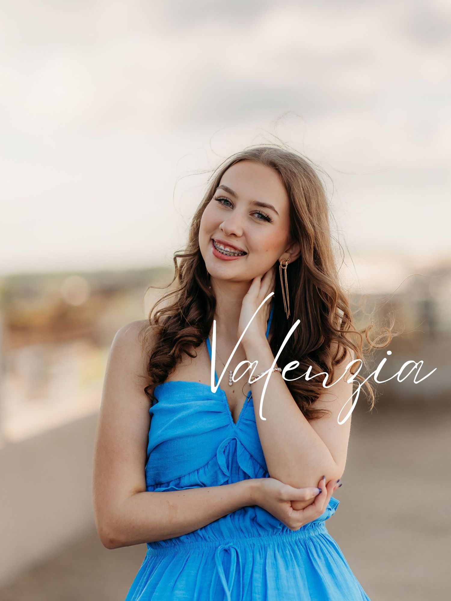 Smiling young woman in a bright blue halter dress poses outdoors with soft blurred background during golden hour.