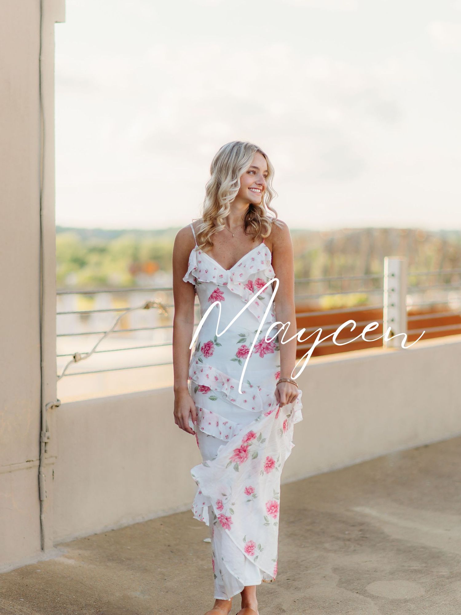 A floral slip dress with spaghetti straps and pink rose print is displayed on a balcony with a scenic countryside view.