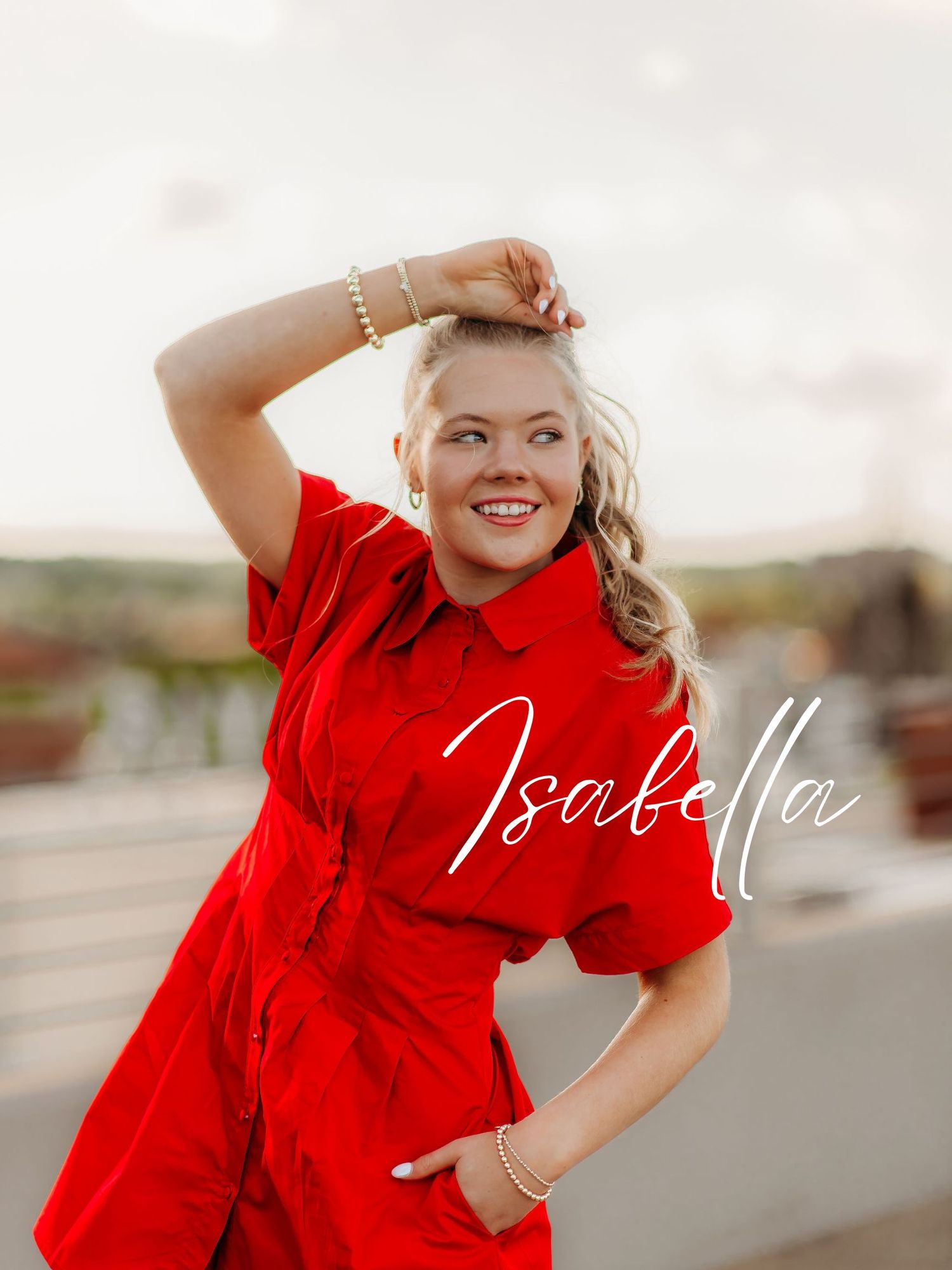 Energetic poses in a vibrant red blouse on a cloudy day next to a parking lot.