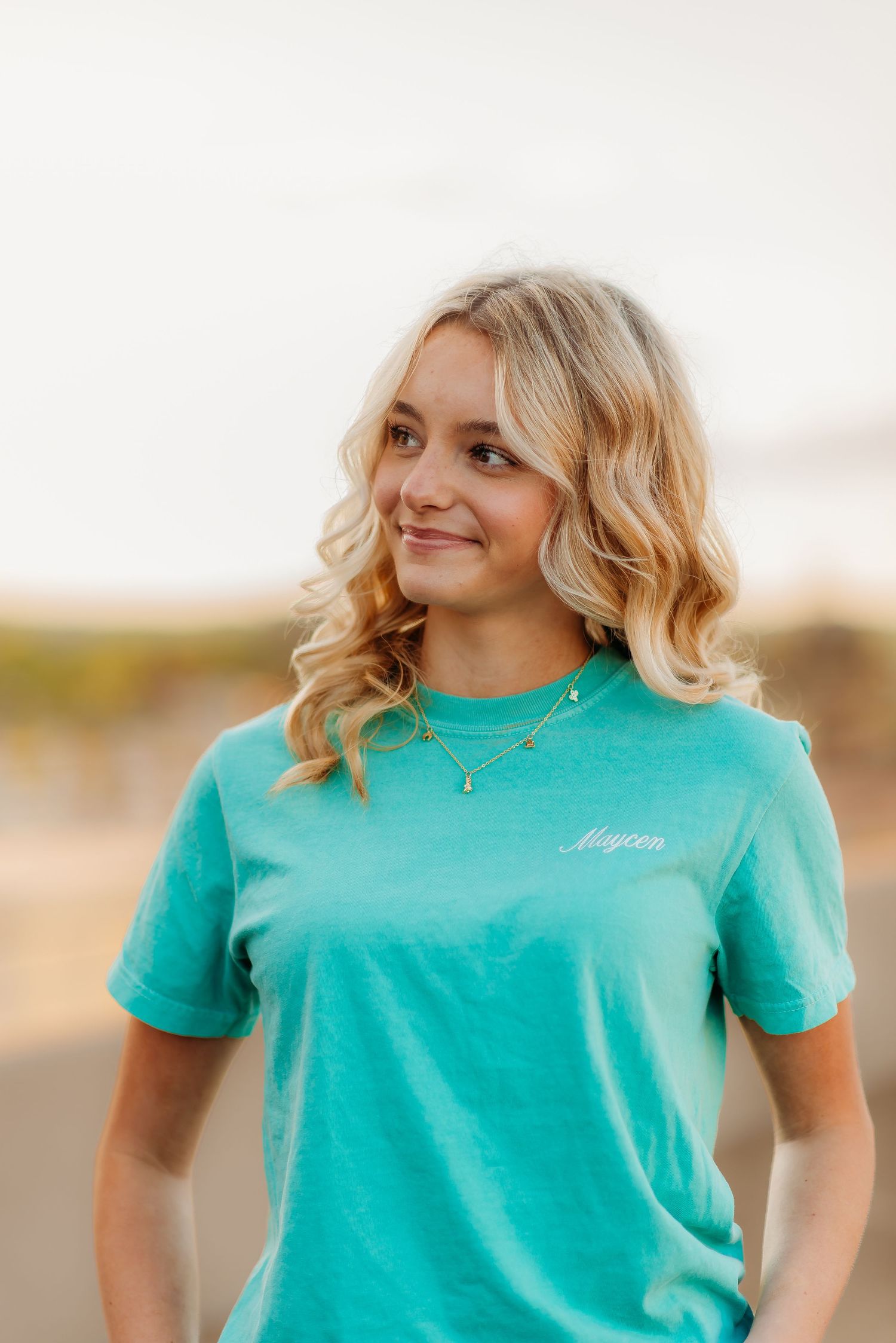 Woman wearing a teal t-shirt smiles outside in sunlight, shown in multiple angles against a blurred background.