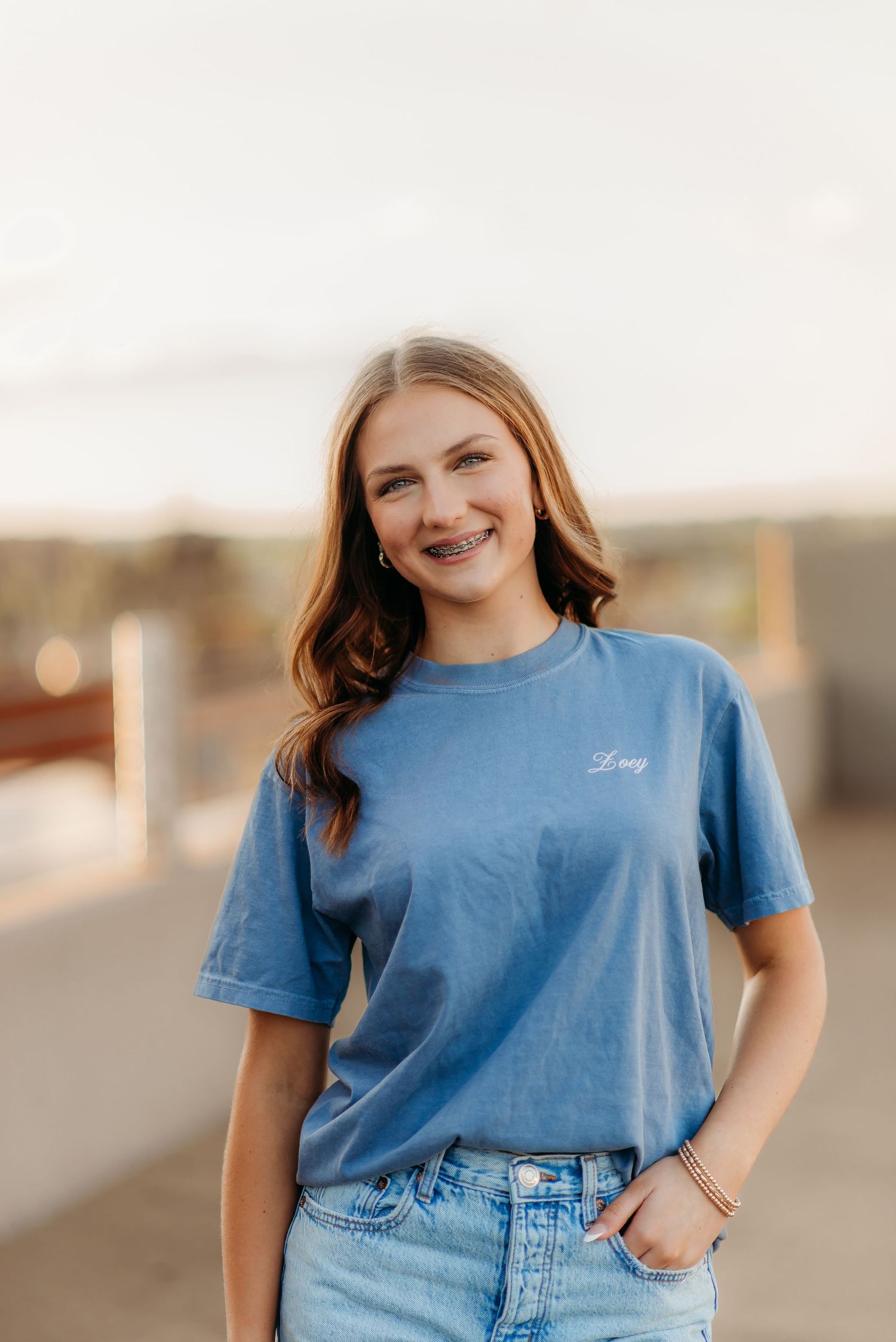 Person wearing a casual blue t-shirt and denim jeans poses outdoors during golden hour.