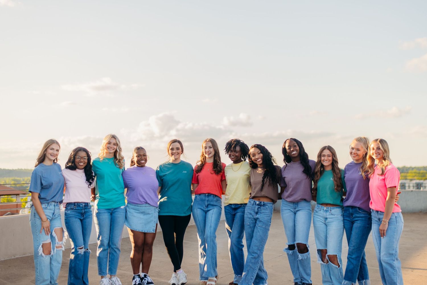 A group of people wearing jeans and coordinated blue outfits stand together outdoors on a sunny day.