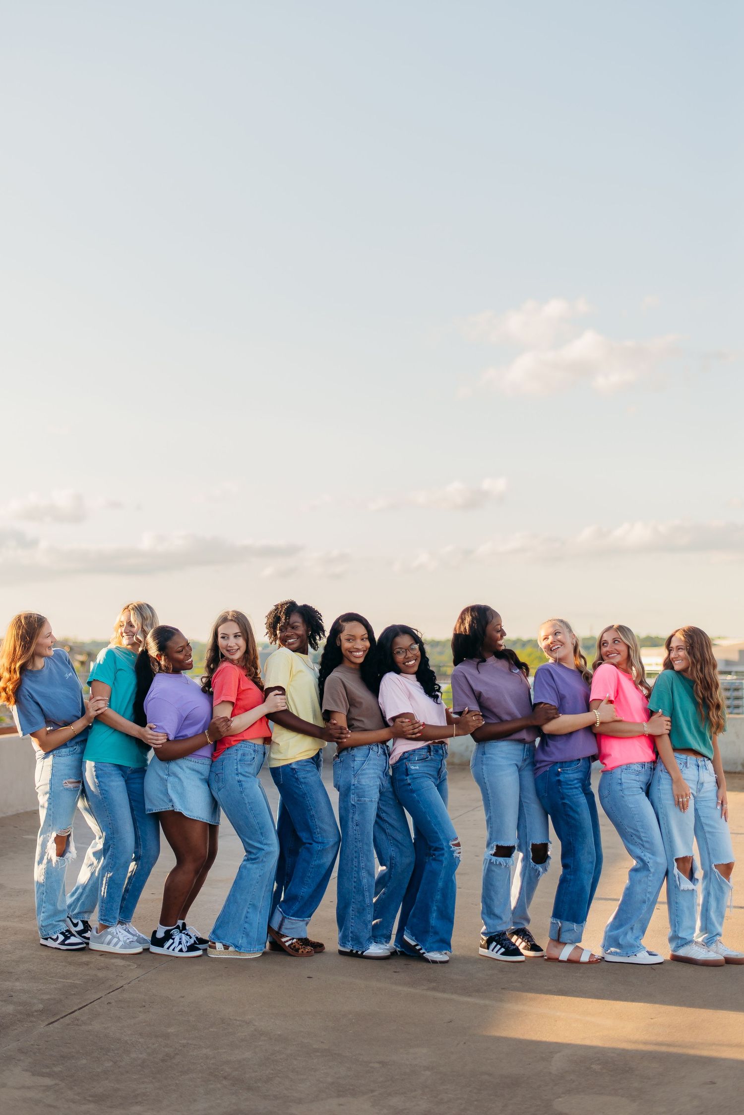 Row of nurses and medical staff in blue scrubs leaning against each other in a human domino formation on a beach at sunset.