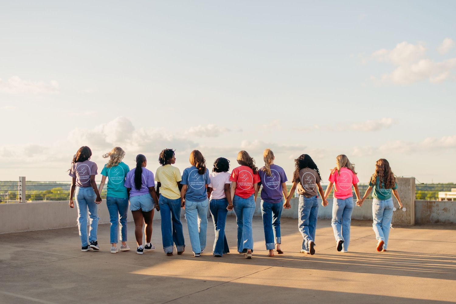 A group of people wearing colorful shirts and blue jeans walking together on a rooftop at sunset.