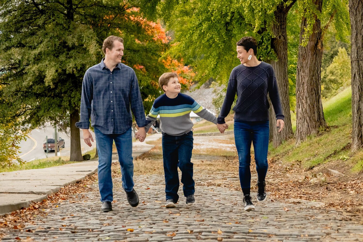 Three people walk together holding hands on a tree-lined path covered in fall leaves on an autumn afternoon. style guide for fall photo