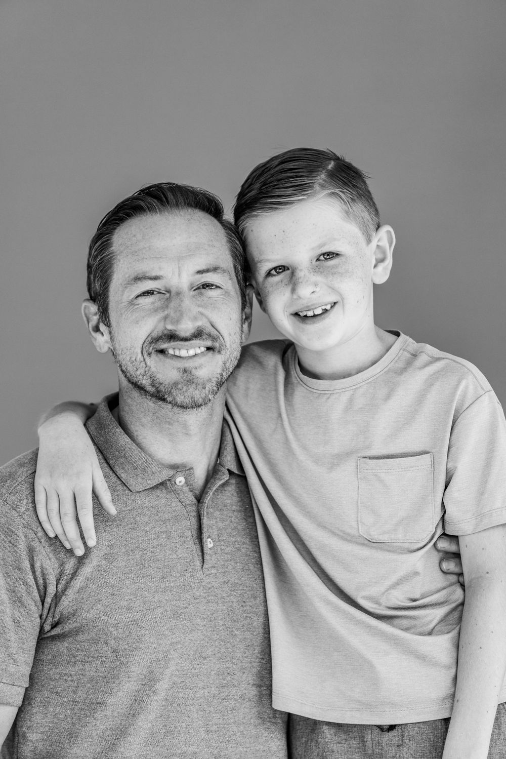 A black and white portrait of an adult and child embracing and smiling at the camera.
