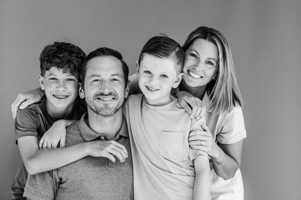 Black and white portrait of a smiling family of four posing together against a plain background.
