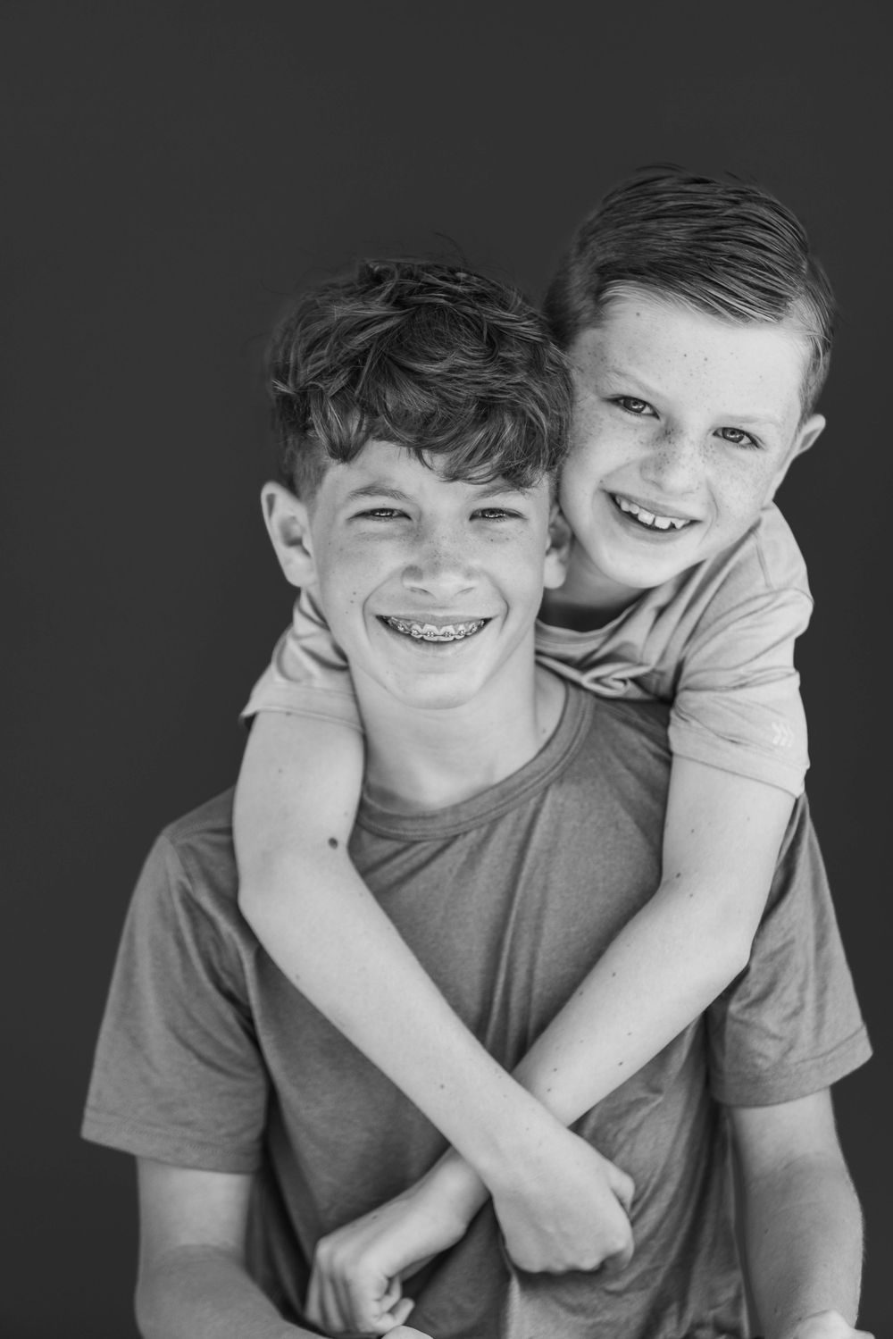 Black and white portrait of two young people hugging and smiling with braces and natural expressions.