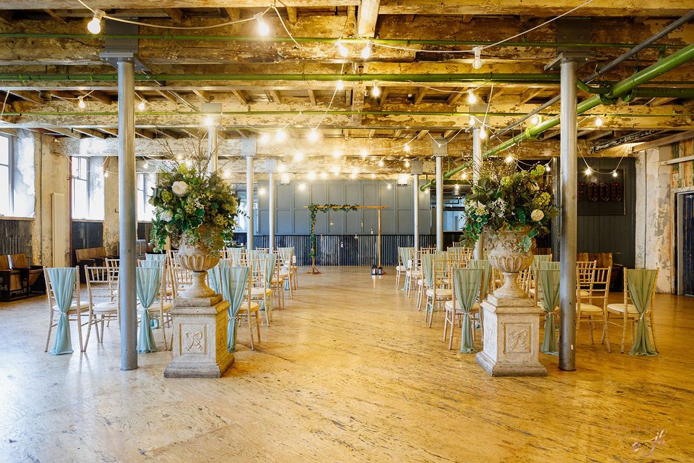 Industrial event space with exposed ceiling beams, wooden floors, and elegant white lanterns along the aisle for ceremonies.