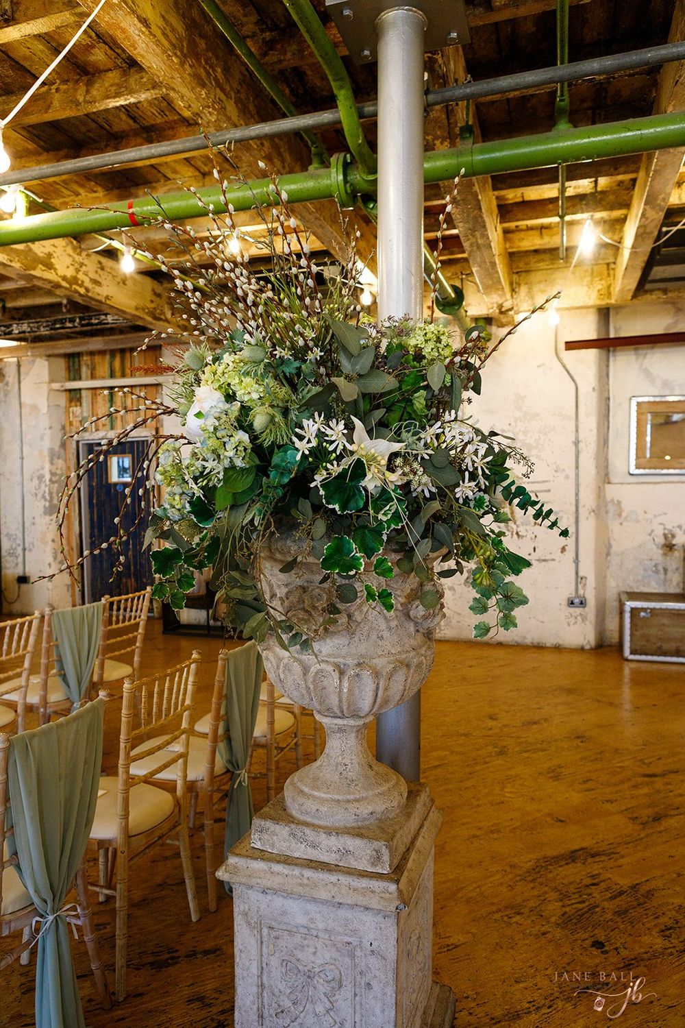 Elegant wedding venue interior with ornate stone pillars, draped fabric, and floral arrangements creating a romantic atmosphere.