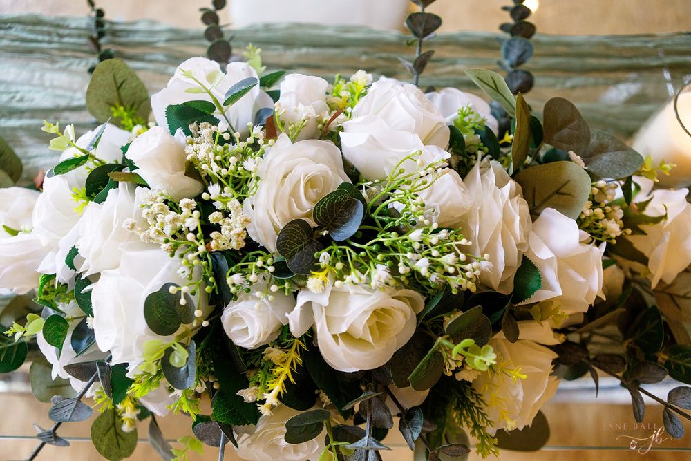Elegant white floral garland with roses and greenery decorates a wedding venue ceiling.