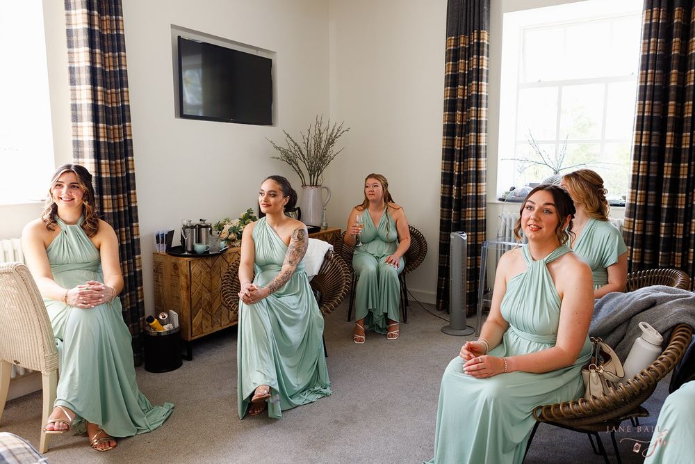Bridesmaids in mint green dresses relaxing and getting ready in a bright room with plaid curtains.