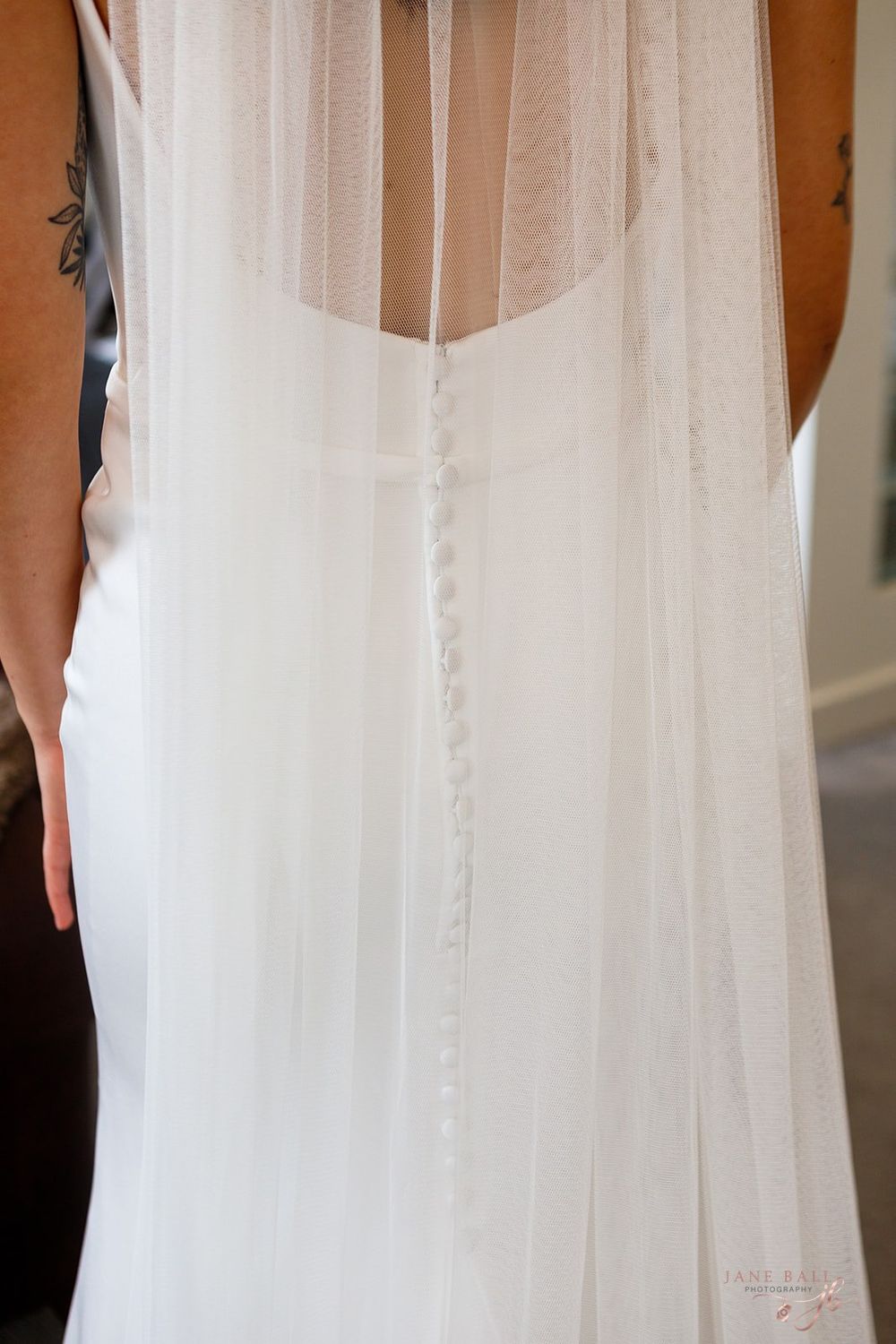 Close-up detail of white wedding dress buttons and delicate tulle veil fabric trailing down the back.