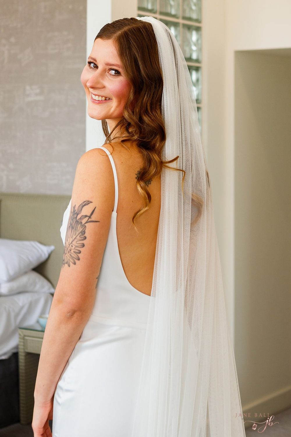Bridal portrait showing a white wedding dress with flowing veil and visible butterfly tattoo.