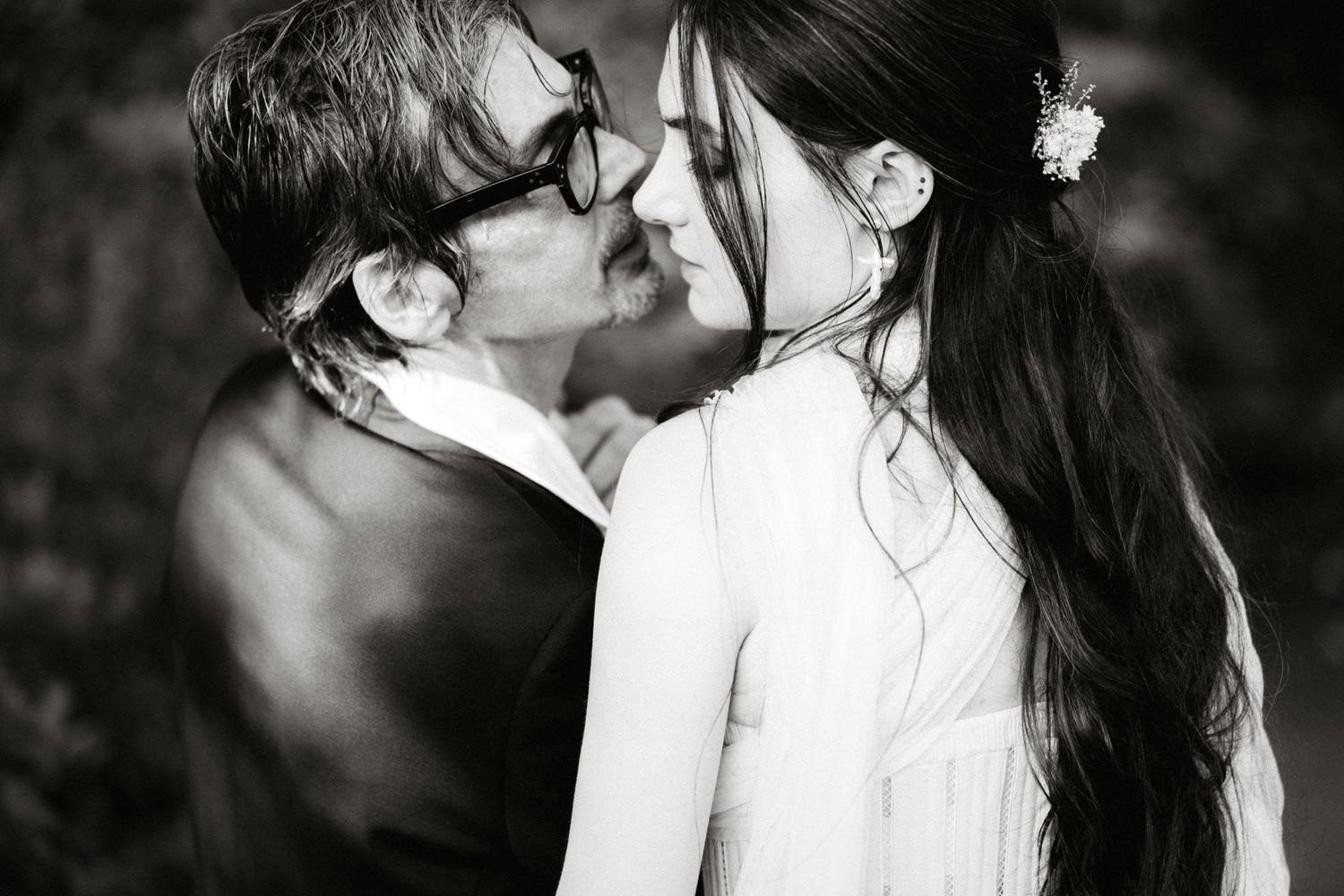 Black and white photo of couple sharing romantic almost-kiss at their wedding ceremony outdoors.
