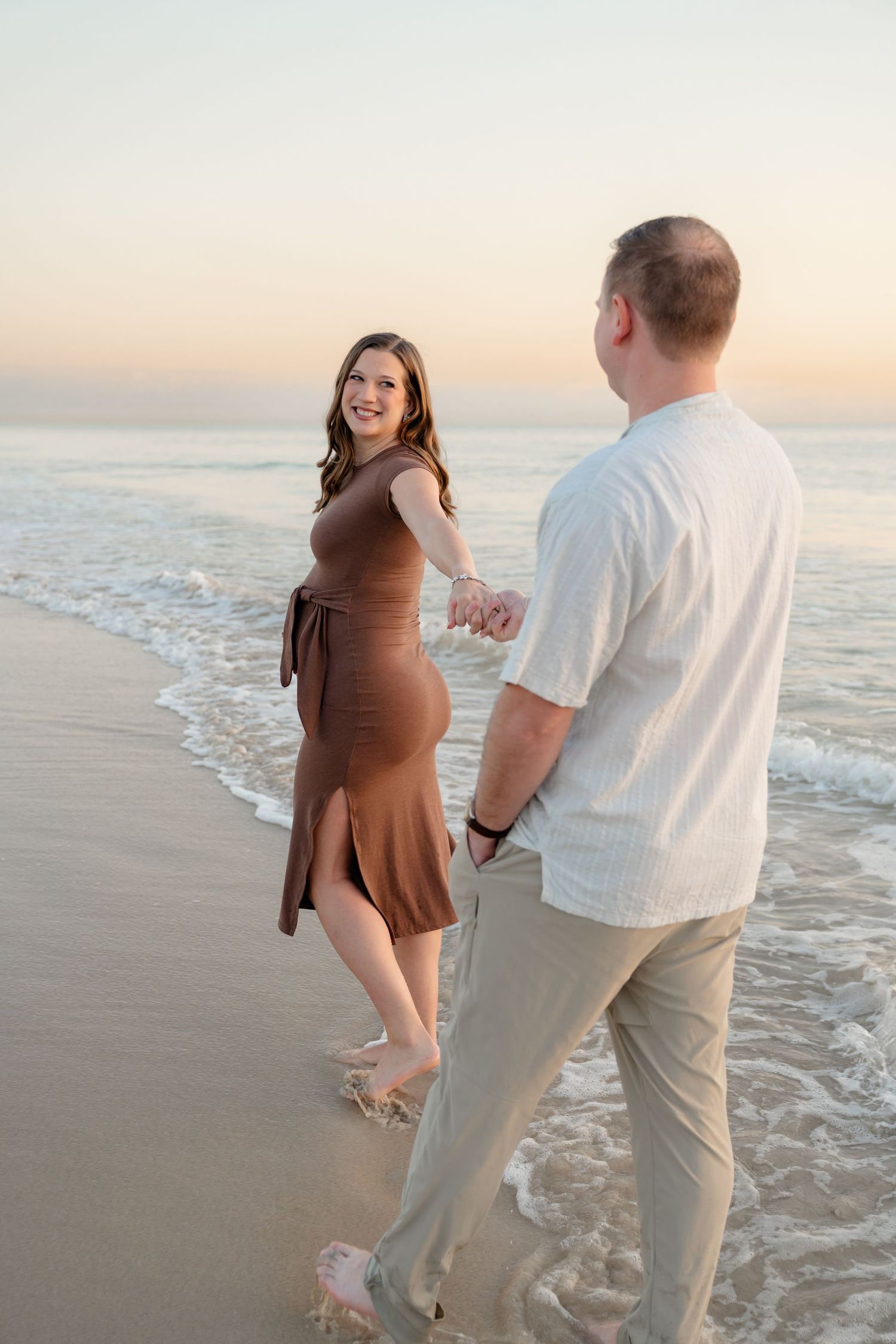 A couple enjoys a romantic moment walking along the beach at sunset with gentle waves rolling onto the shore.