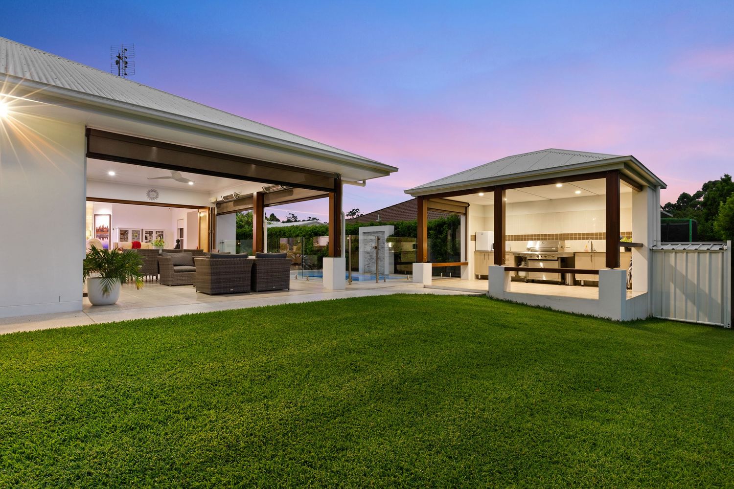 Spacious outdoor entertaining area with covered patio and gazebo on manicured lawn at dusk.