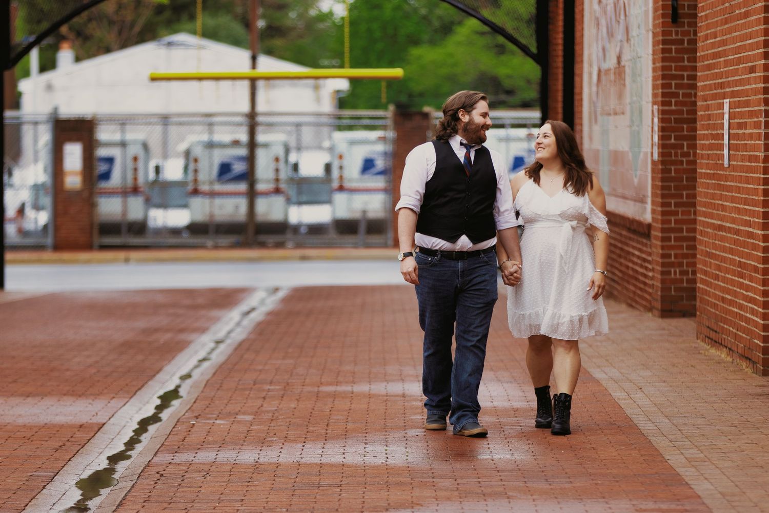 A couple walks together on a brick sidewalk beside a red brick building in an urban setting.