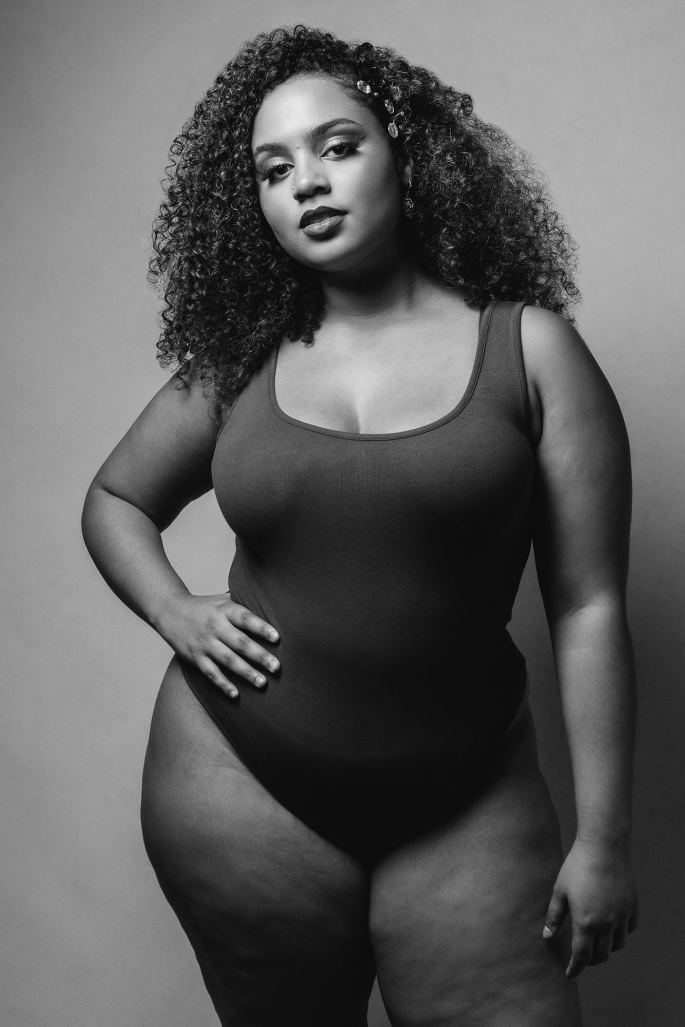 A series of black and white fashion portraits showing a plus-size model in a black tank top posing confidently.
