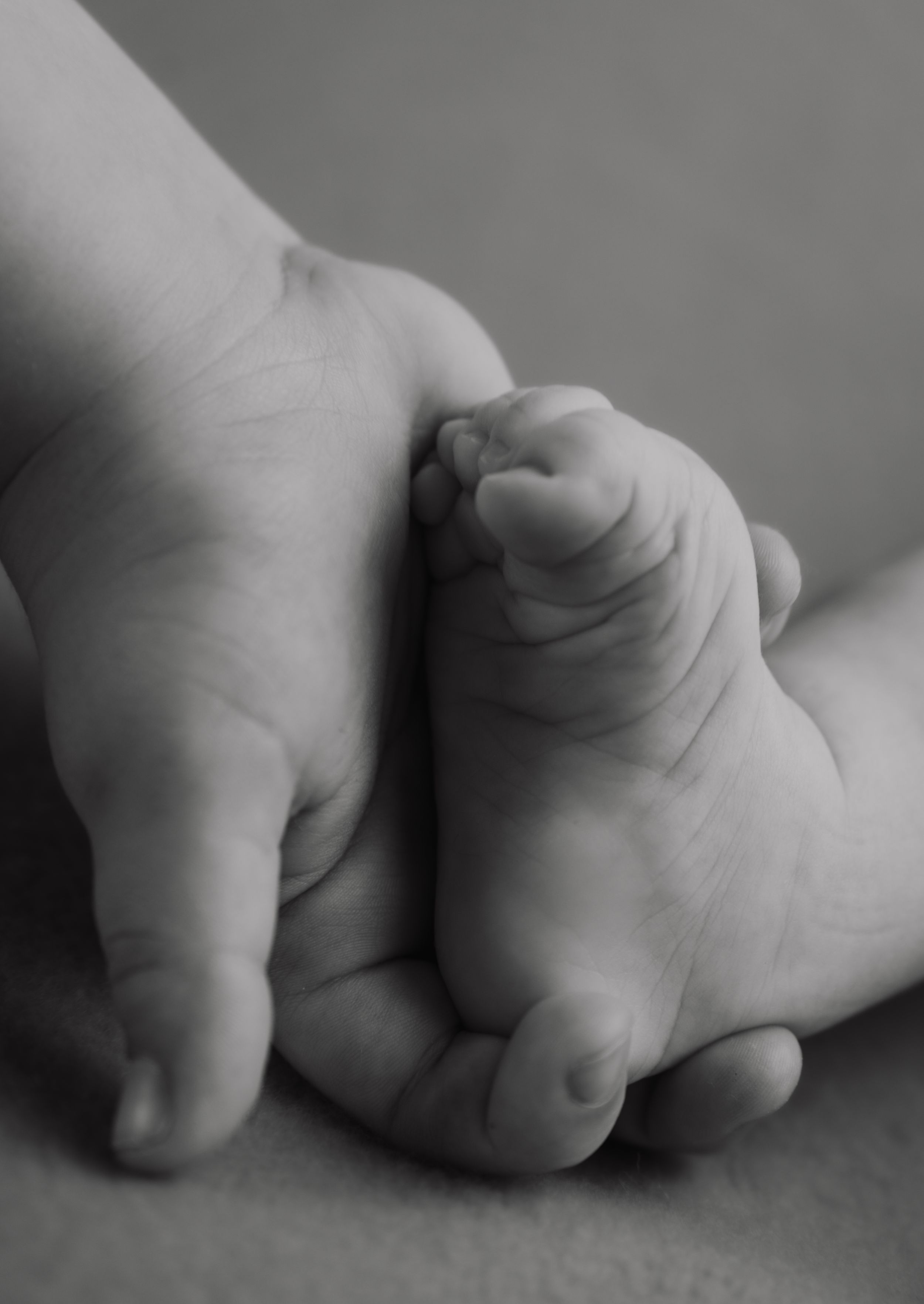 Black and white close-up of an adult hand gently holding a tiny newborn baby foot.