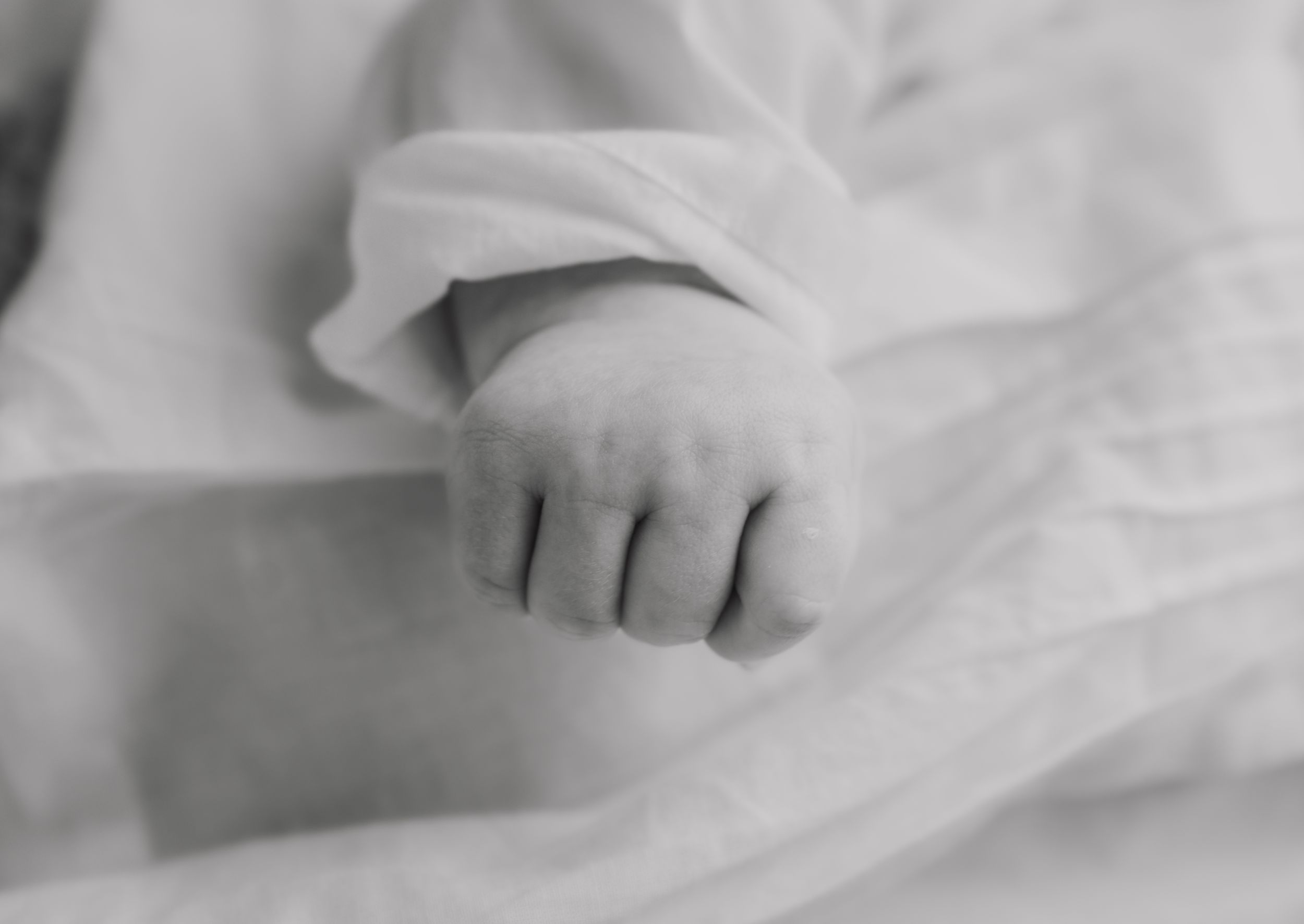 Black and white close-up of a newborn baby's tiny hand resting on white fabric.