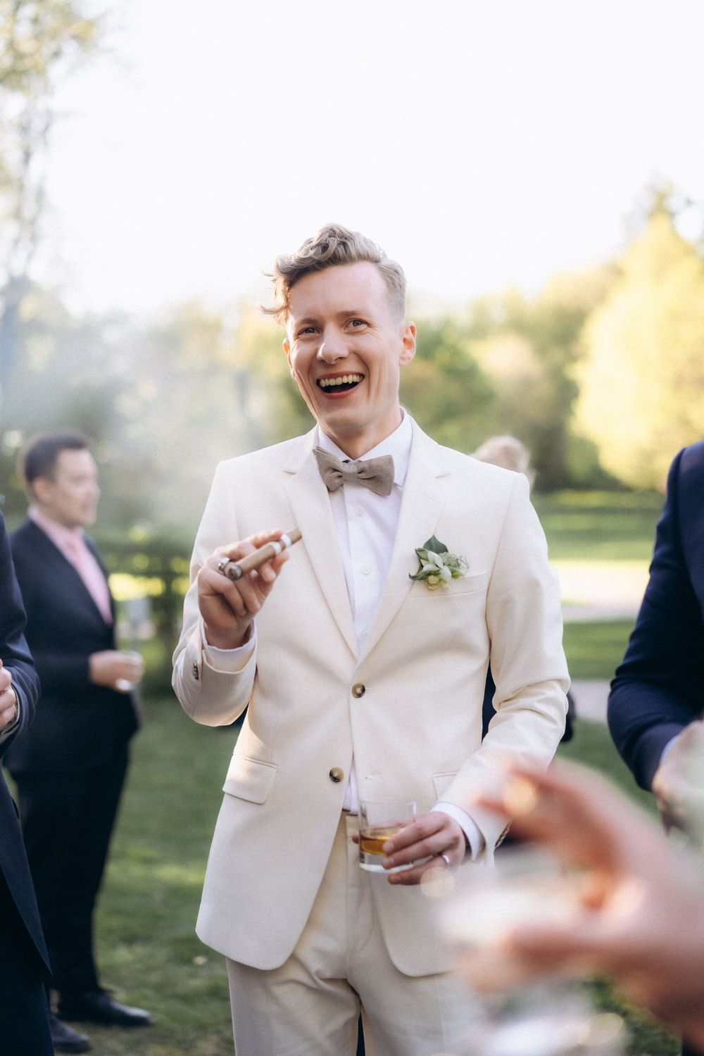 groom smiling with wiskey glass during outdoor wedding reception Espoon Kartano natural candid wedding photography
