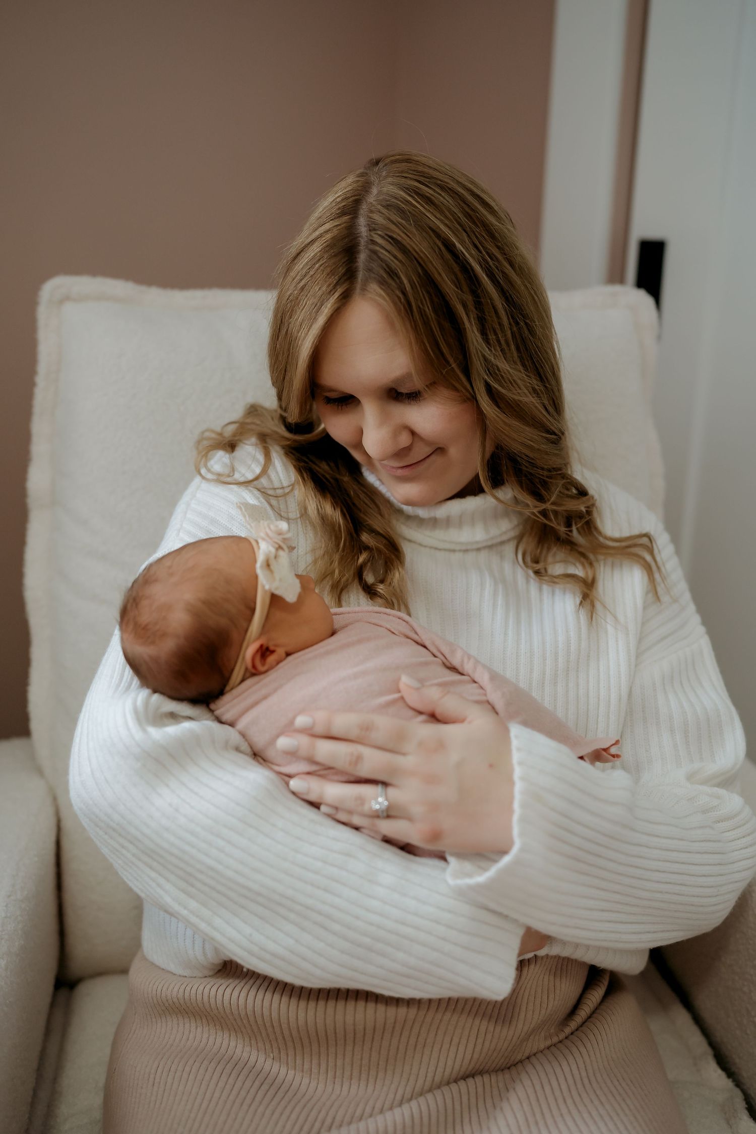 A mother in a white sweater holds and cuddles her newborn baby in a series of tender moments on a couch.