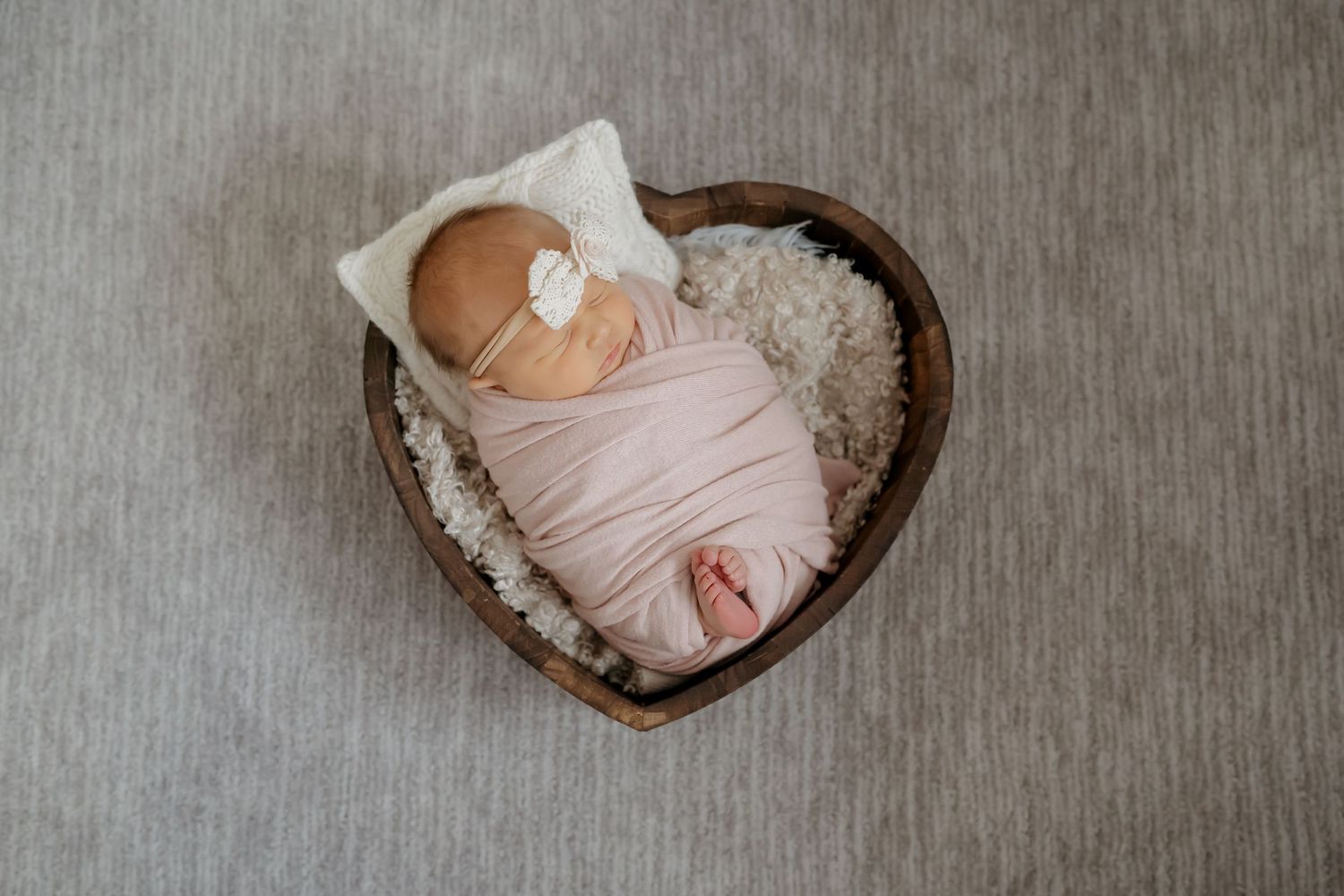 A collage of newborn photography showing a sleeping baby in pink swaddle blanket positioned in wooden heart-shaped bowls.