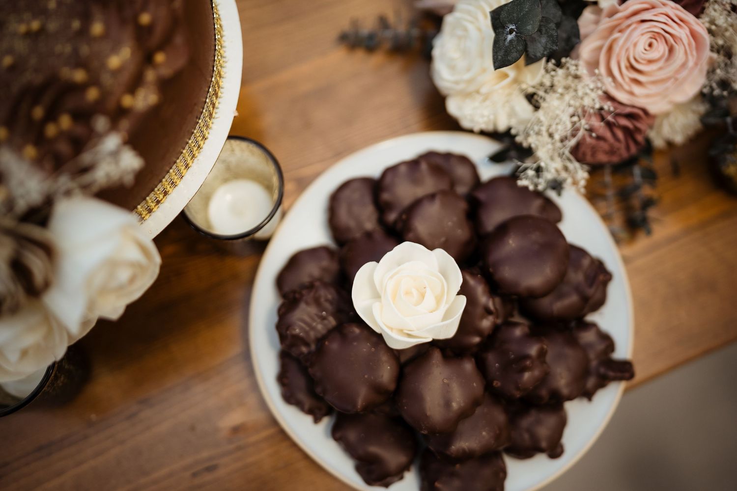 Chocolate covered desserts and pink roses arranged on a rustic wooden surface for an elegant event display.
