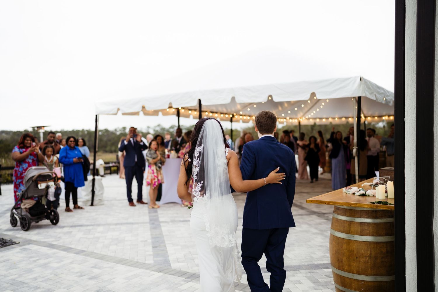 Wedding guests gather on a patio with wine barrels and coastal views during an outdoor celebration.