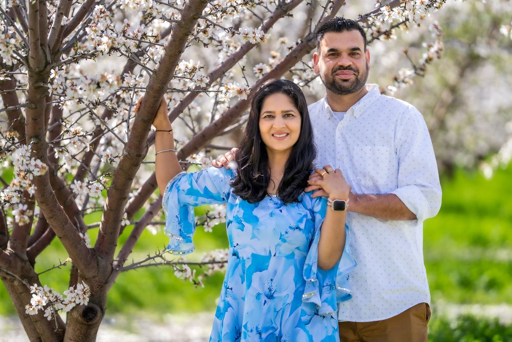 A couple stands together under blooming cherry blossom trees on a spring day in a park.