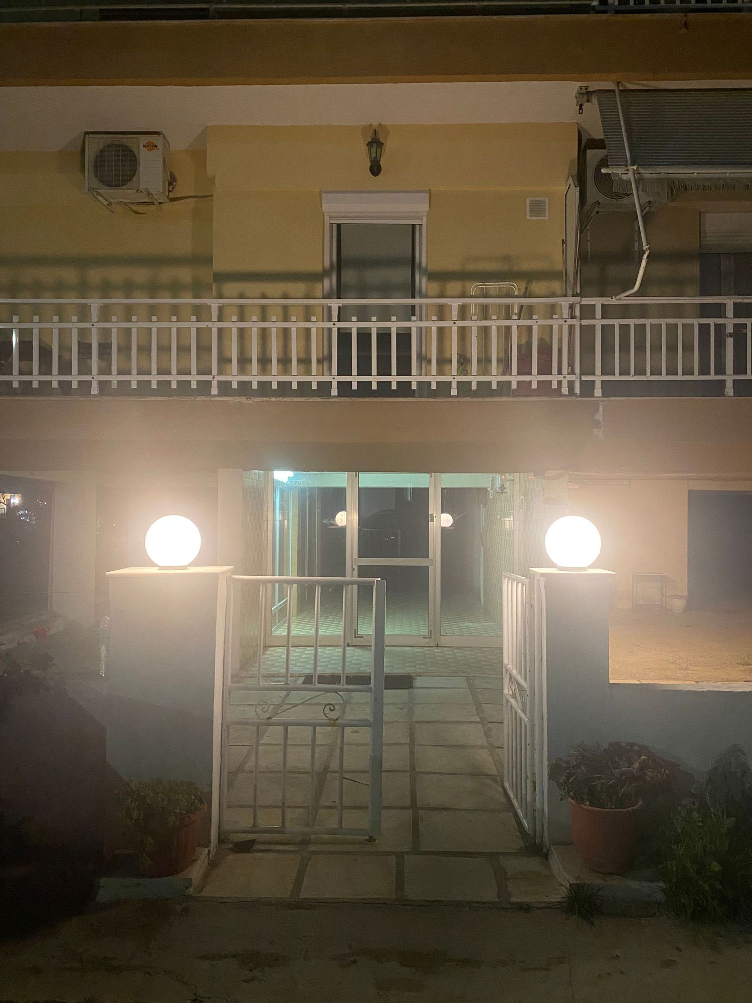 White gate and railing illuminated by outdoor lights at night creating a welcoming entrance to a residential property.