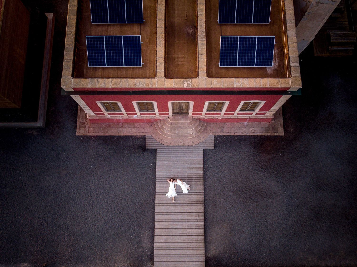 Aerial drone shot of a bride and groom standing on a wooden pier next to a modern building - Artistic wedding photography in Fuerteventura