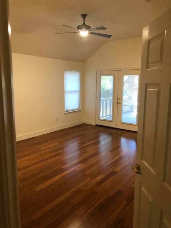 Empty room with hardwood floors, white walls, ceiling fan, and glass door leading to balcony with natural light coming in.