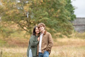A couple shares a romantic moment in a field with autumn trees and soft lighting in the background.