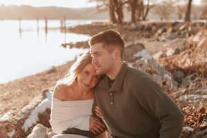 A couple shares an intimate moment together on a rocky shoreline during golden hour sunset.