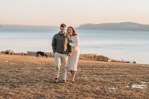 A couple walks together on a grassy coastal hillside during golden hour with ocean views in the background.