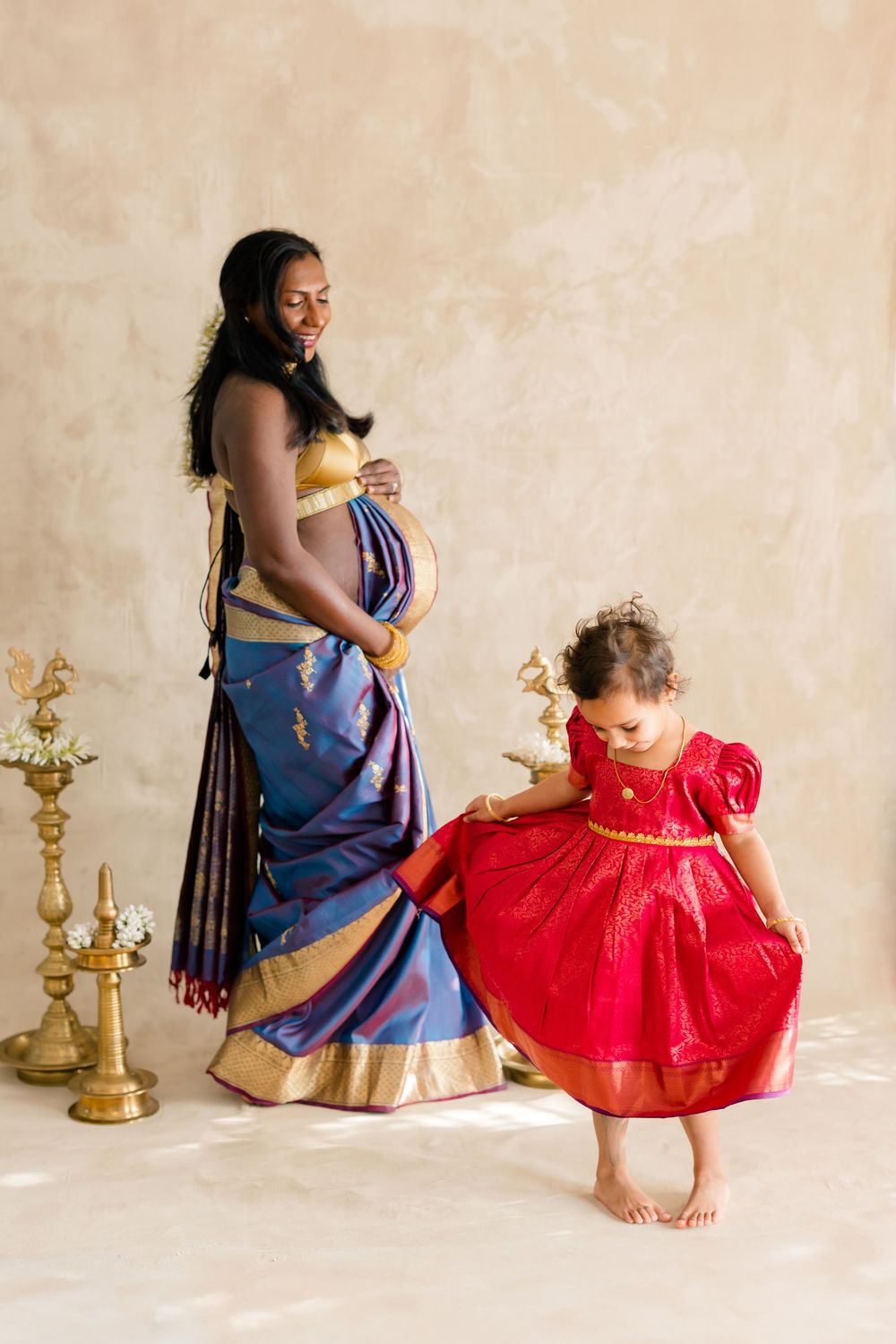 A parent and child in traditional Indian attire share tender moments while sitting against a neutral backdrop.