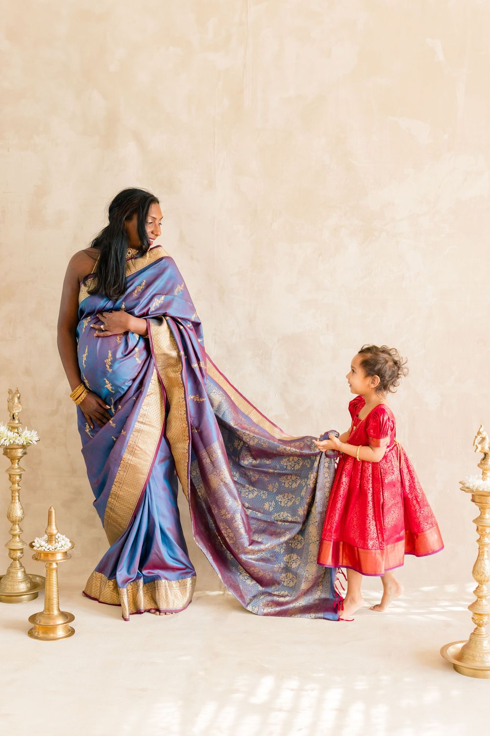 A series of tender moments between a woman in a blue sari and a child in a red dress with brass lamps in the background.