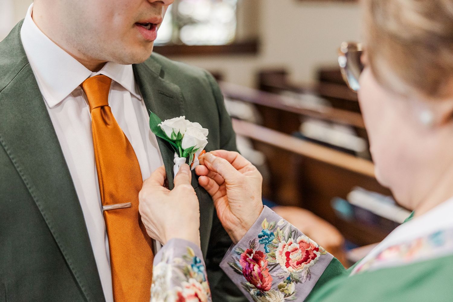 A boutonniere being pinned to a green suit jacket with an orange tie during a formal event preparation.
