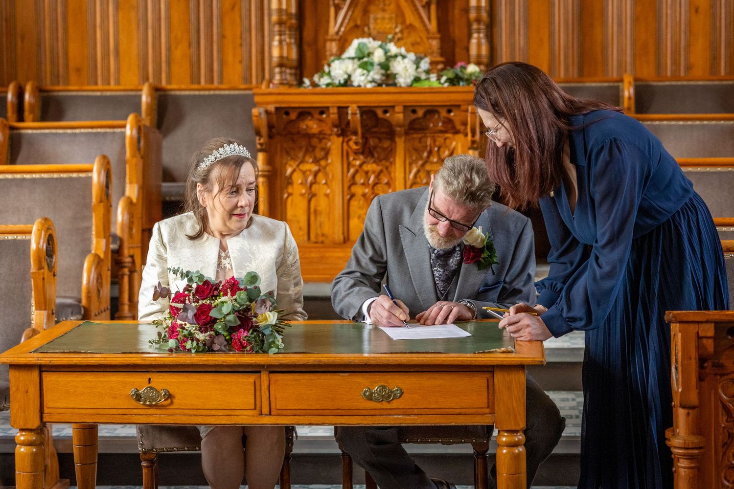 Groom signing the wedding register at Southport Town Hall as bride watches, registrar guiding at wooden desk.
