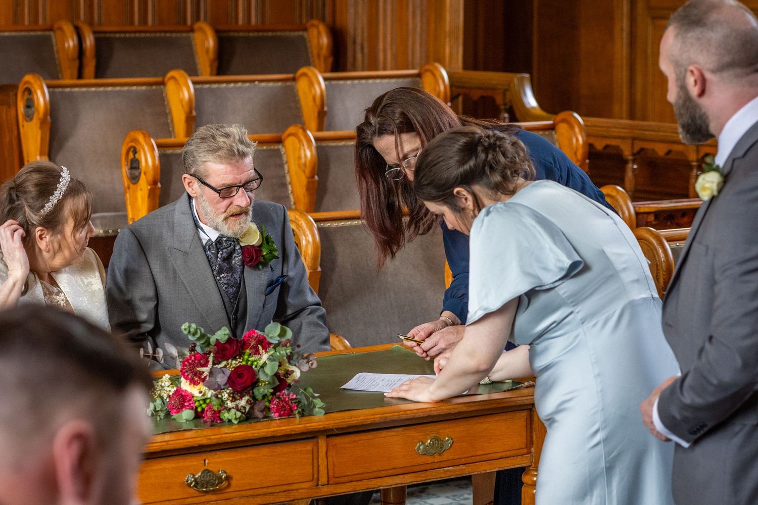 Bridesmaid signing wedding register beside bride and groom at Southport Town Hall ceremony in Merseyside