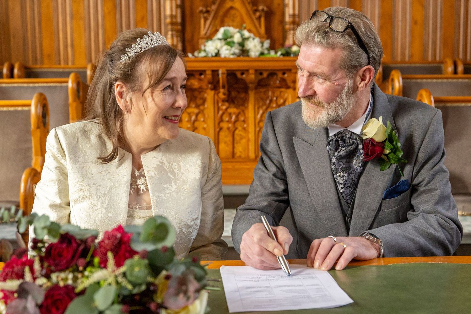 Groom signs, bride watches.Groom signing the wedding register at Southport Town Hall as bride smiles across the desk in Lancashire ceremony