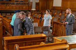 Older groom hugs guest after signing the register at Southport Town Hall wedding ceremony, documentary wedding photography