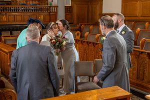 Bride hugs bridesmaid daughter holding bouquet inside Southport Town Hall ceremony room, natural wedding photographer